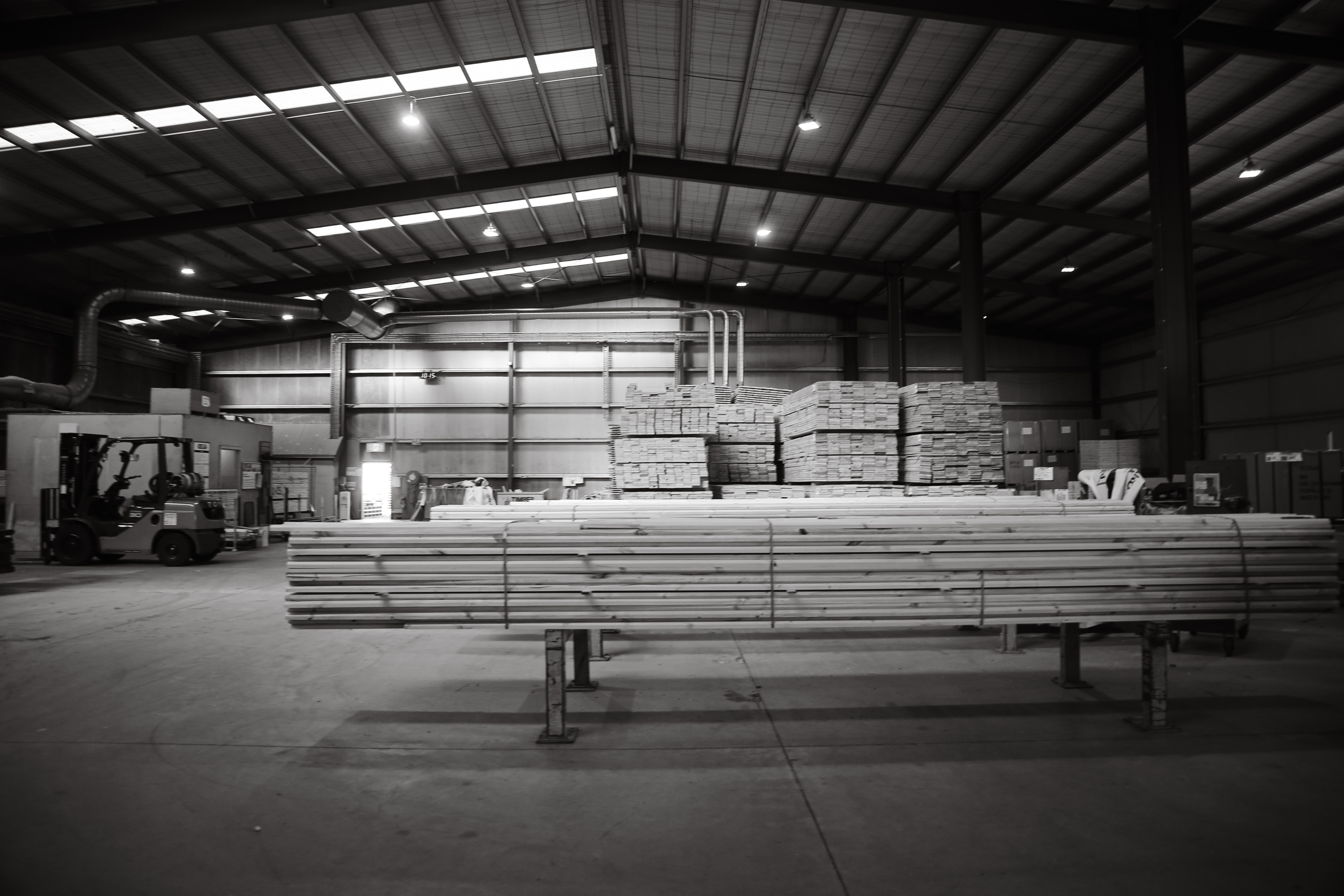 Two workers reviewing a clipboard in a sunlit timber warehouse, black and white