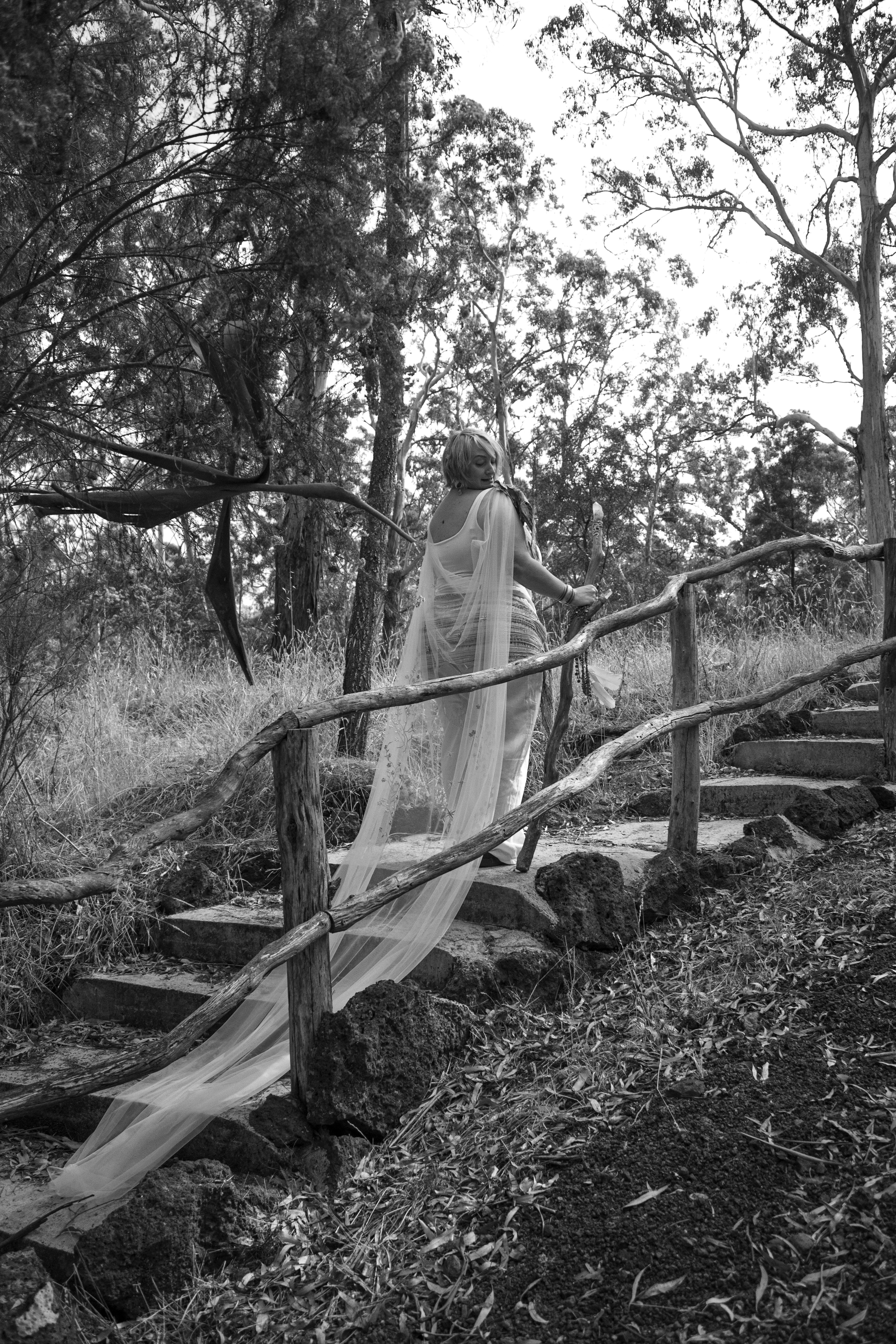 Woman in white veil ascending stone steps through bush, portrait
