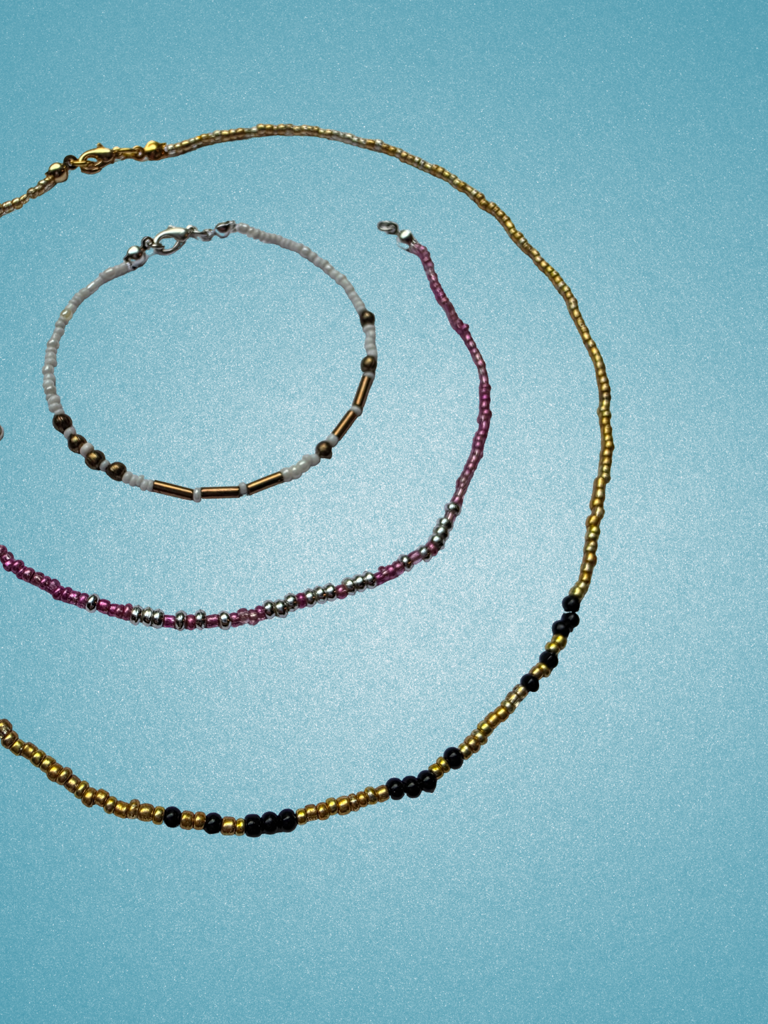 Beaded necklaces and bracelets arranged in concentric spirals against a blue background