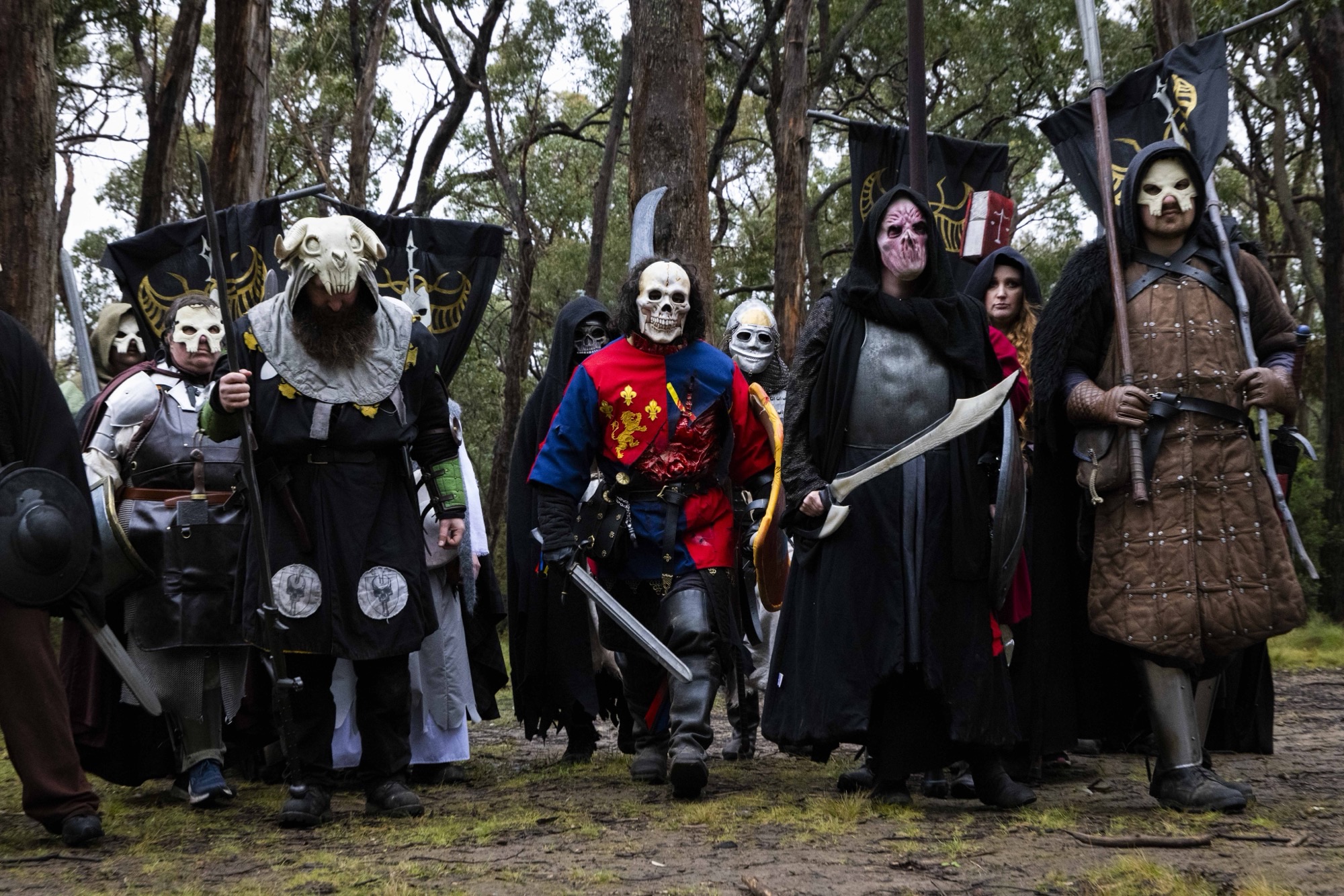 A group of players costumed as the undead army — skull masks, black robes and dark banners — march through a forest at the Pomborneit event