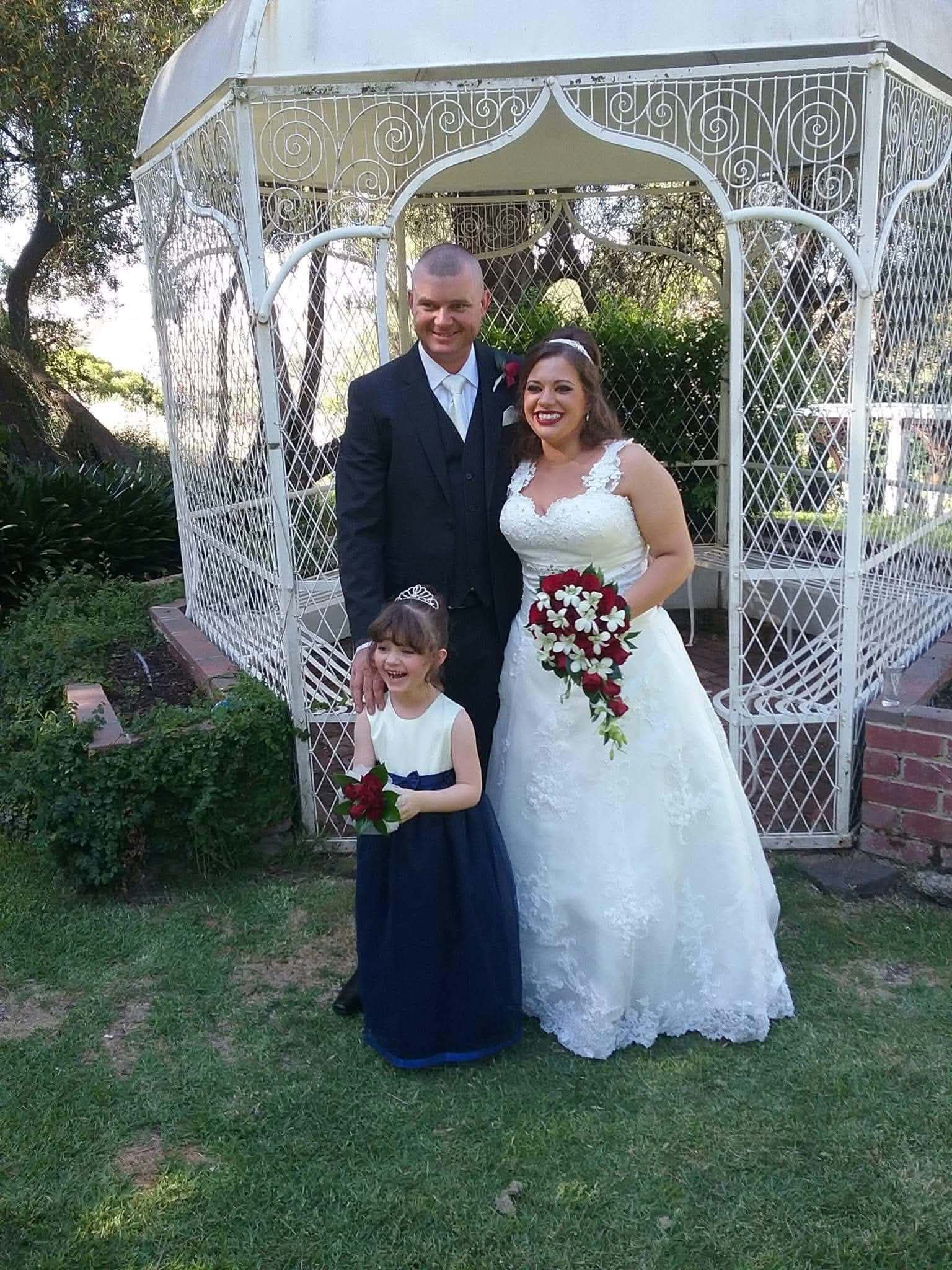 Ronnie and her husband on their wedding day, daughter Millie in a navy dress between them, in front of a white gazebo