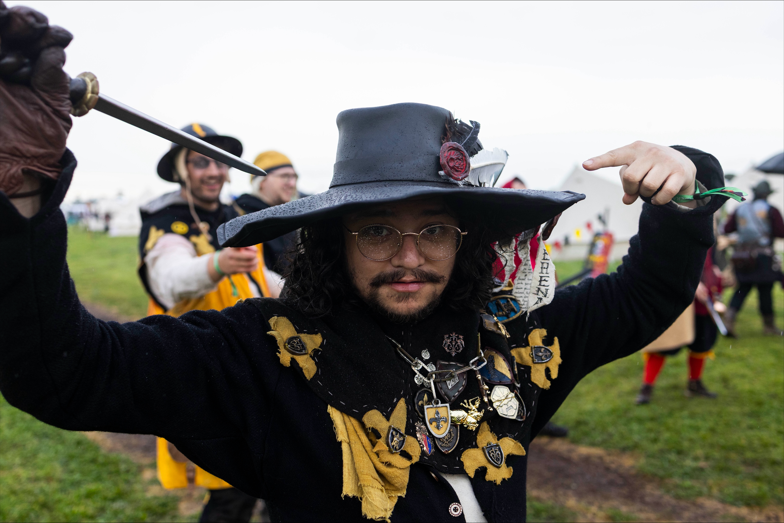 A costumed Swordcraft player in a black hat and decorated armour raises a sword during the Pomborneit event